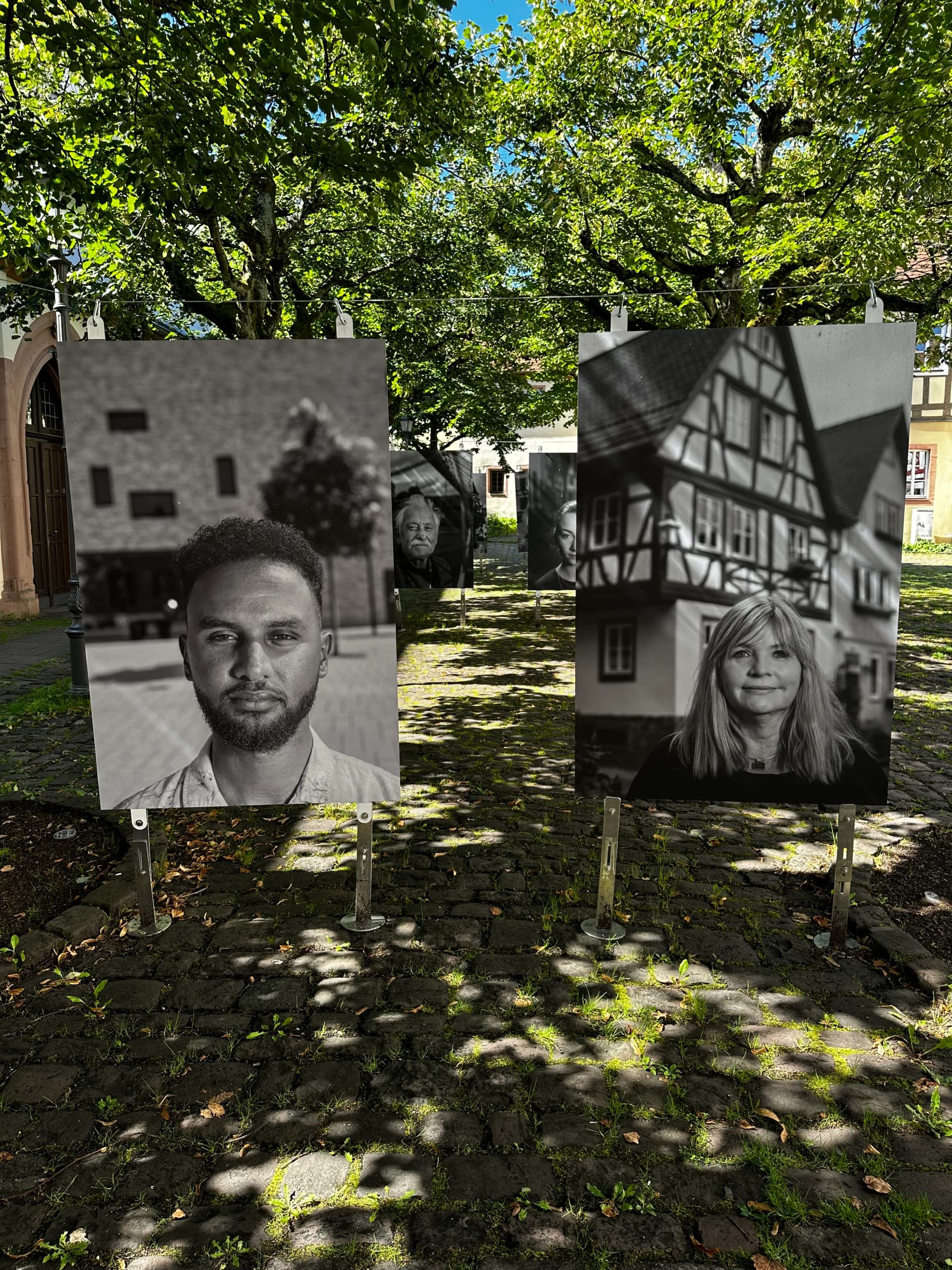 Ausstellungstafeln mit Schwarz-Weiß-Porträtfotos an einer Steinmauer im Freien aufgestellt