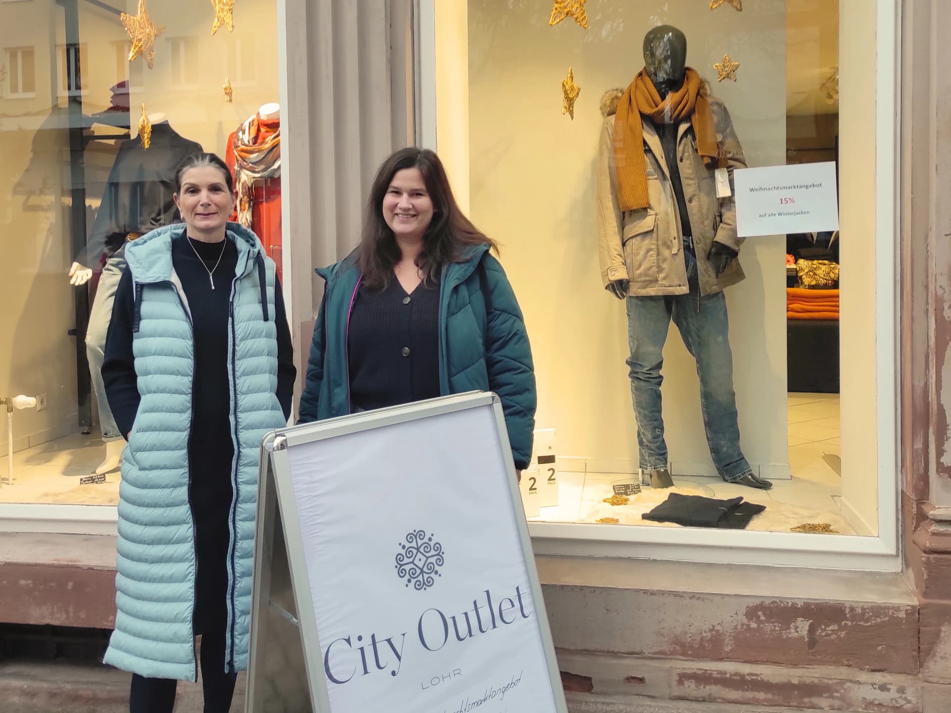 Zwei Frauen in Winterjacken stehen vor dem Schaufenster des City Outlet Lohr mit weihnachtlich dekorierter Auslage