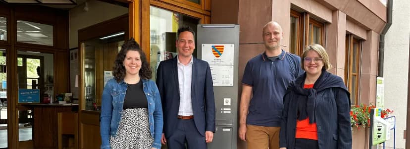 Vier Personen stehen vor dem Eingang des Rathauses mit dem Stadtwappen an der Fassade.