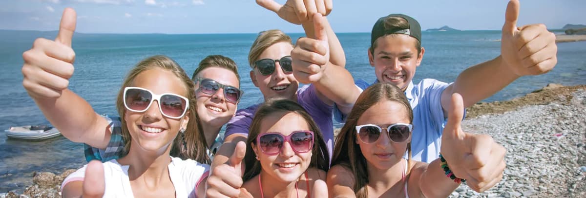 Gruppe Jugendlicher am Strand zeigt lachend die Daumen nach oben