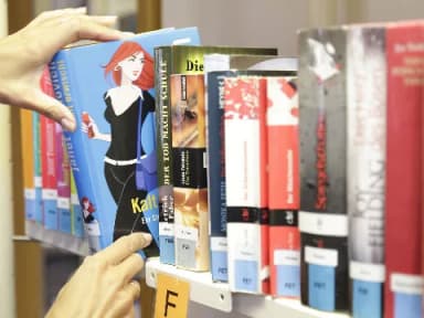 Hände nehmen ein Buch aus einem Regal mit verschiedenen Büchern in einer Bibliothek.
