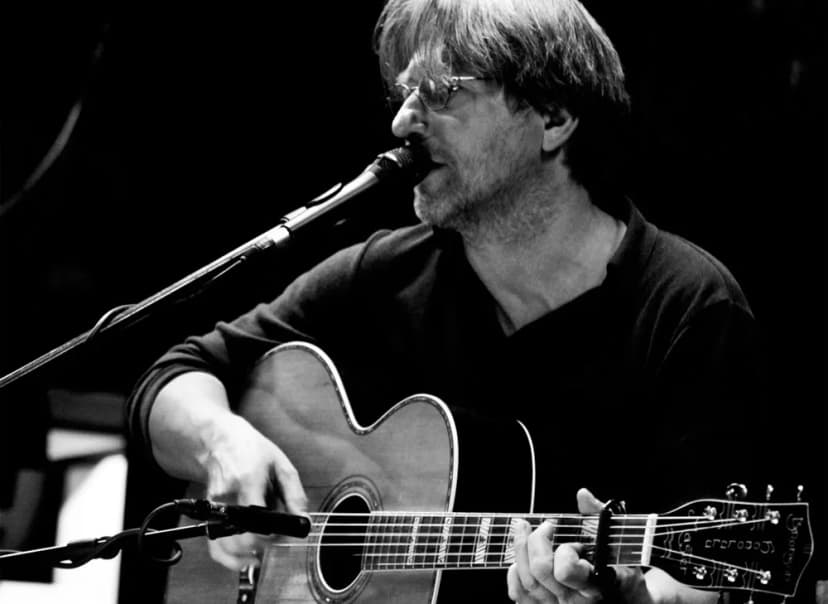 Mann mit Brille singt an einem Mikrofon und spielt akustische Gitarre, Schwarzweißaufnahme