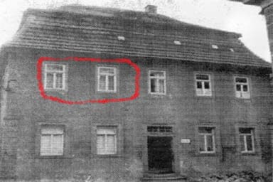 Historische Schwarz-Weiß-Aufnahme eines Wohnhauses, zwei Fenster im Obergeschoss rot markiert