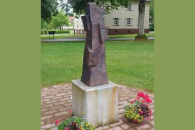 Abstrakte Bronzeskulptur 'Turm der Erinnerung' auf Steinsockel in einer Grünanlage