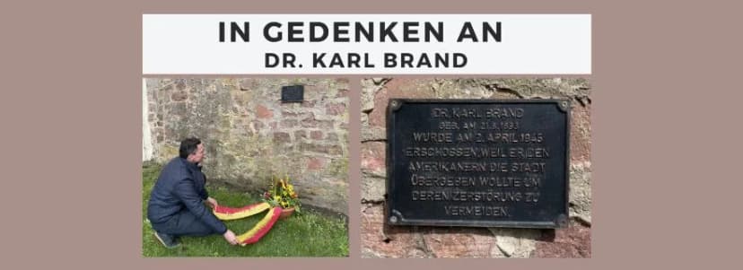 Mann kniet mit Kranz vor Gedenktafel für Dr. Karl Brand, daneben Tafel mit Inschrift zu dessen Erschießung 1945