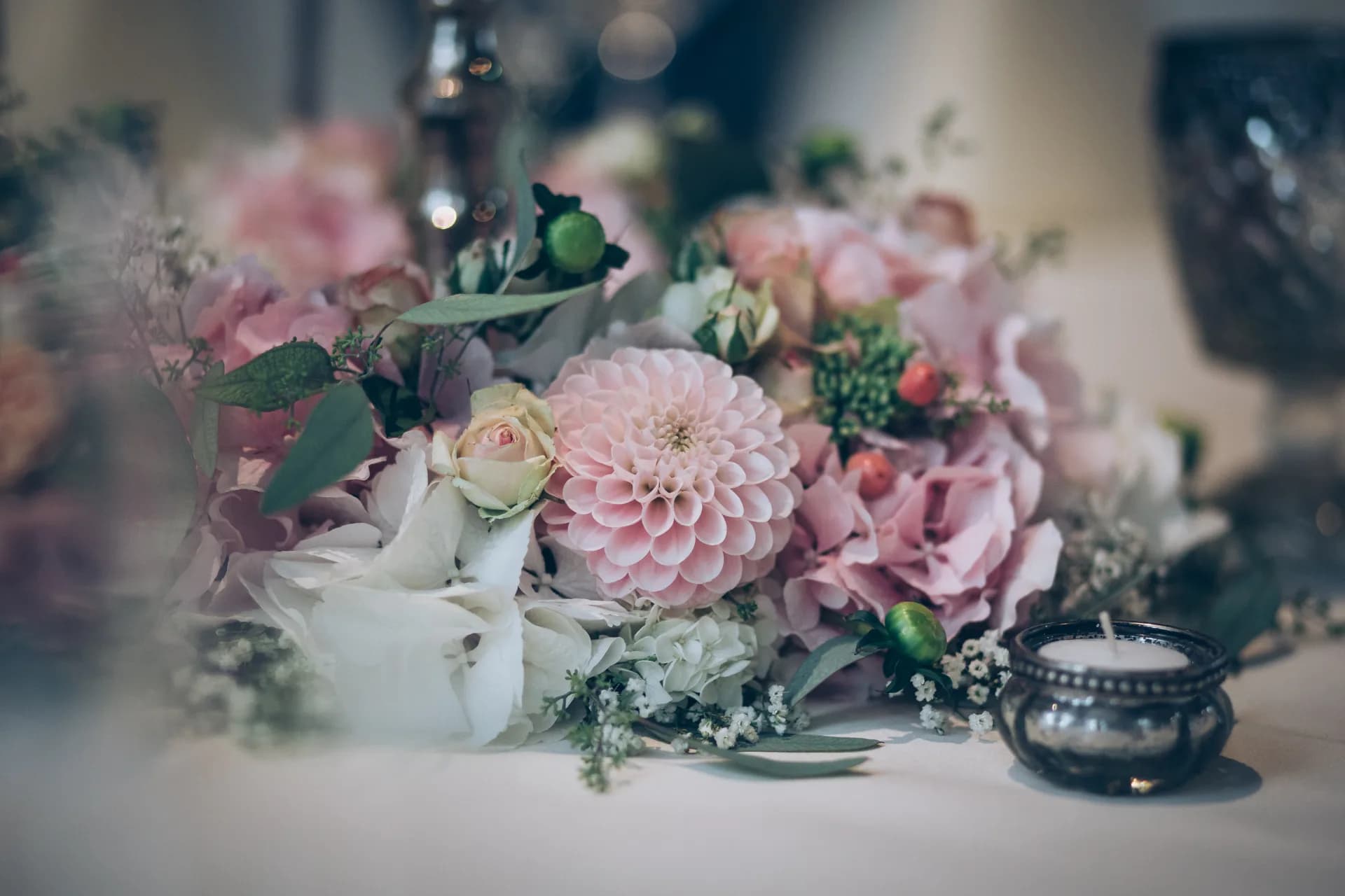 Blumendekoration mit rosa Dahlie, Rosen und Hortensien neben einem kleinen Teelicht auf einem Tisch