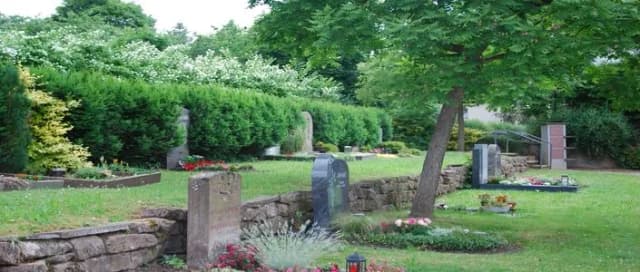 Friedhof mit Grabsteinen, Rasenflächen, Hecken und Bäumen