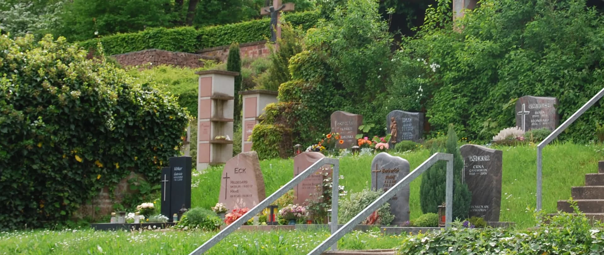 Grabsteine an einem hangartigen Friedhof mit Blumenschmuck und Grünpflanzen zwischen Treppenstufen