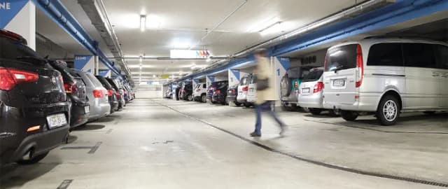 Parkende Autos in einem Parkhaus mit Person, die zwischen den Fahrzeugen entlanggeht