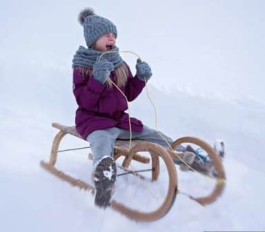 Ein Kind sitzt auf einem Schlitten und rodelt in einer Winterlandschaft