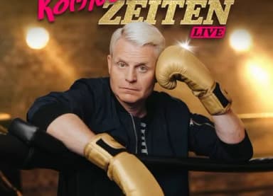 Werbeplakat 'Komische Zeiten Live': Mann mit goldenen Boxhandschuhen lehnt in einem Boxring