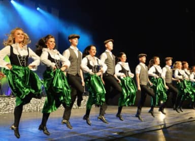 Tanzgruppe in irischer Tracht mit grünen Röcken tanzt synchron auf einer Bühne