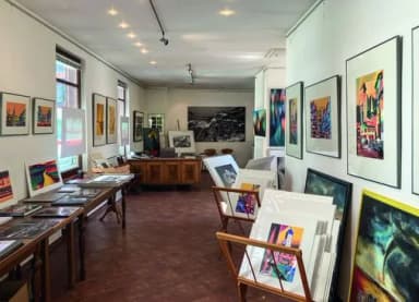 Galerieraum mit zahlreichen bunten Gemälden und Grafiken an den Wänden sowie auf Tischen und Staffeleien ausgestellt