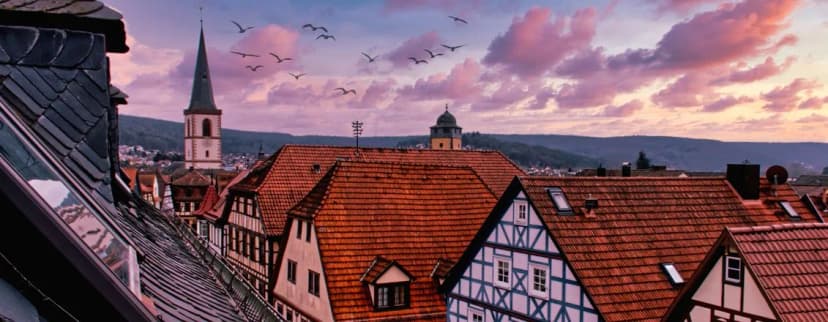 Blick über die Ziegeldächer und Fachwerkhäuser der Altstadt mit Kirchturm bei Abenddämmerung, Vögel im Himmel