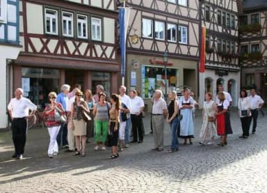 Gruppe von Menschen bei einer Stadtführung vor Fachwerkhäusern auf gepflastertem Marktplatz