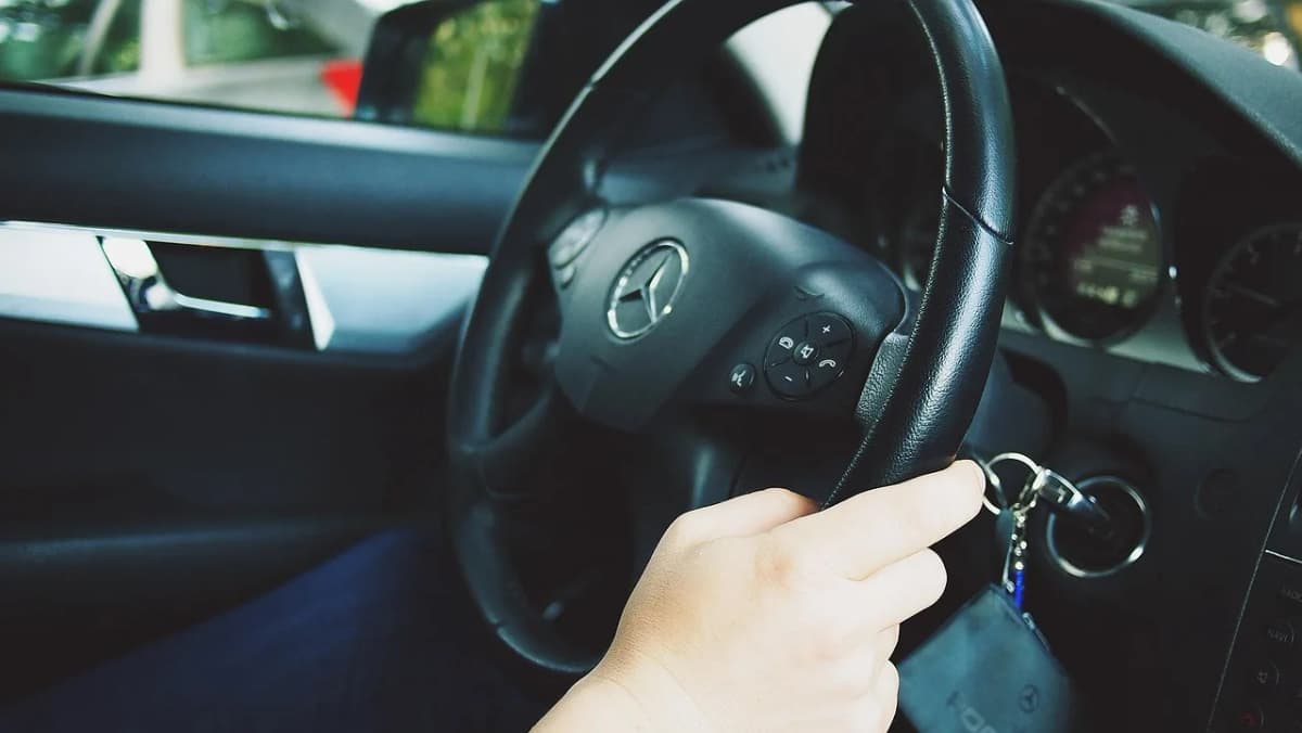 Eine Hand ist an einem Lenkrad in einem Auto zu sehen.