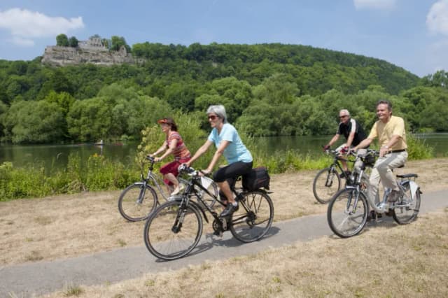Radfahrer die am Main in Karlstadt fahren. Im Hintergrund ist noch die Burgruine Karlsburg zu sehen.
