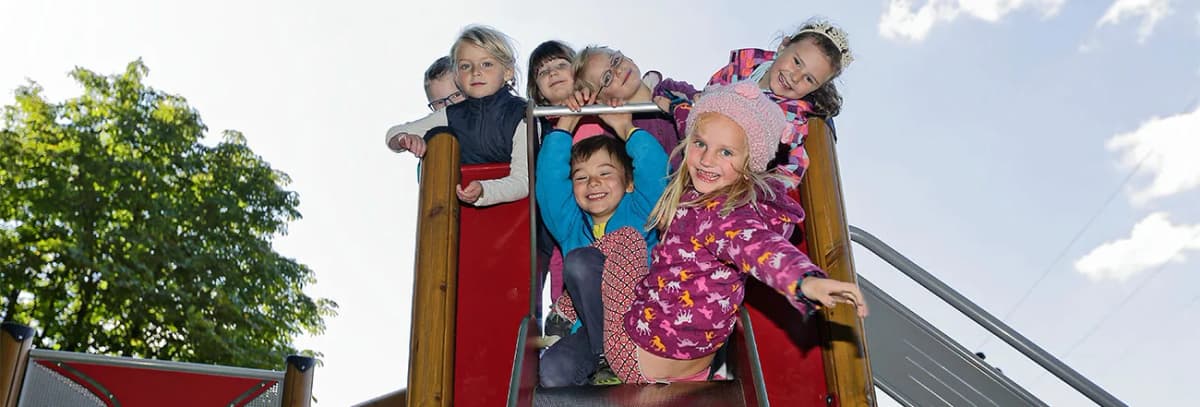 Gruppe von Kindern lacht auf einer Spielplatzrutsche