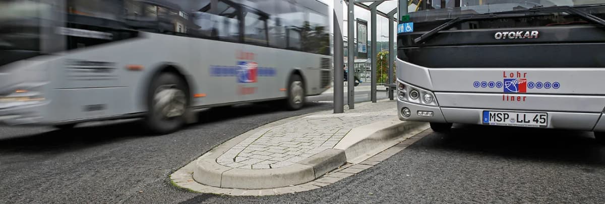 Zwei Busse an einer Bushaltestelle mit überdachter Wartefläche und gepflasterter Fahrgastinsel