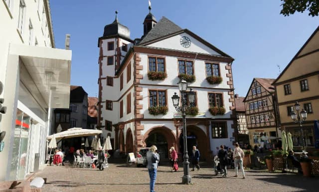 Historisches Rathaus mit Turm und Uhr am Marktplatz, davor Passanten und Straßencafés