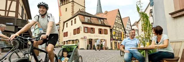 Radfahrer mit Kinderanhänger und Café-Gäste auf dem Kopfsteinpflaster der Altstadt mit Fachwerkhäusern und Kirchturm