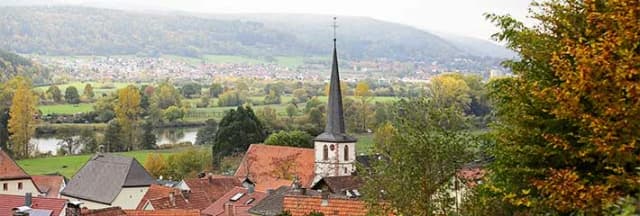 Blick über Dächer und Kirchturm auf Fluss und Hügellandschaft im Herbst
