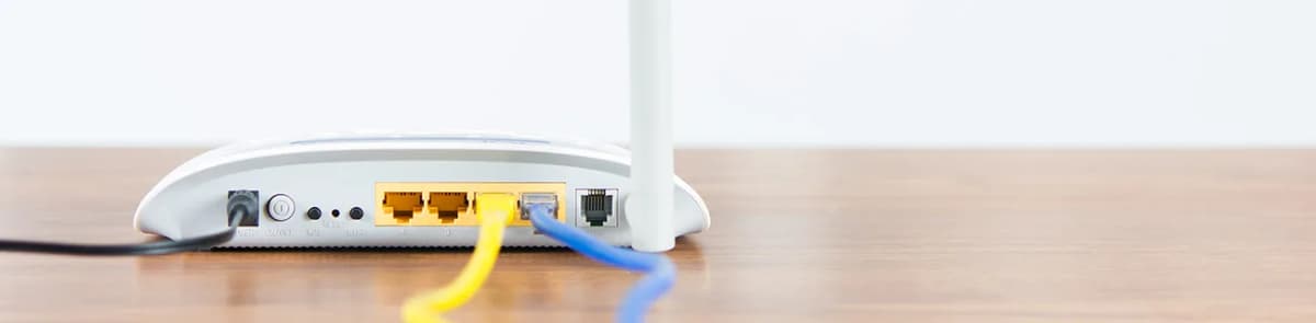 Rückseite eines WLAN-Routers mit angeschlossenen Netzwerkkabeln auf einem Holztisch