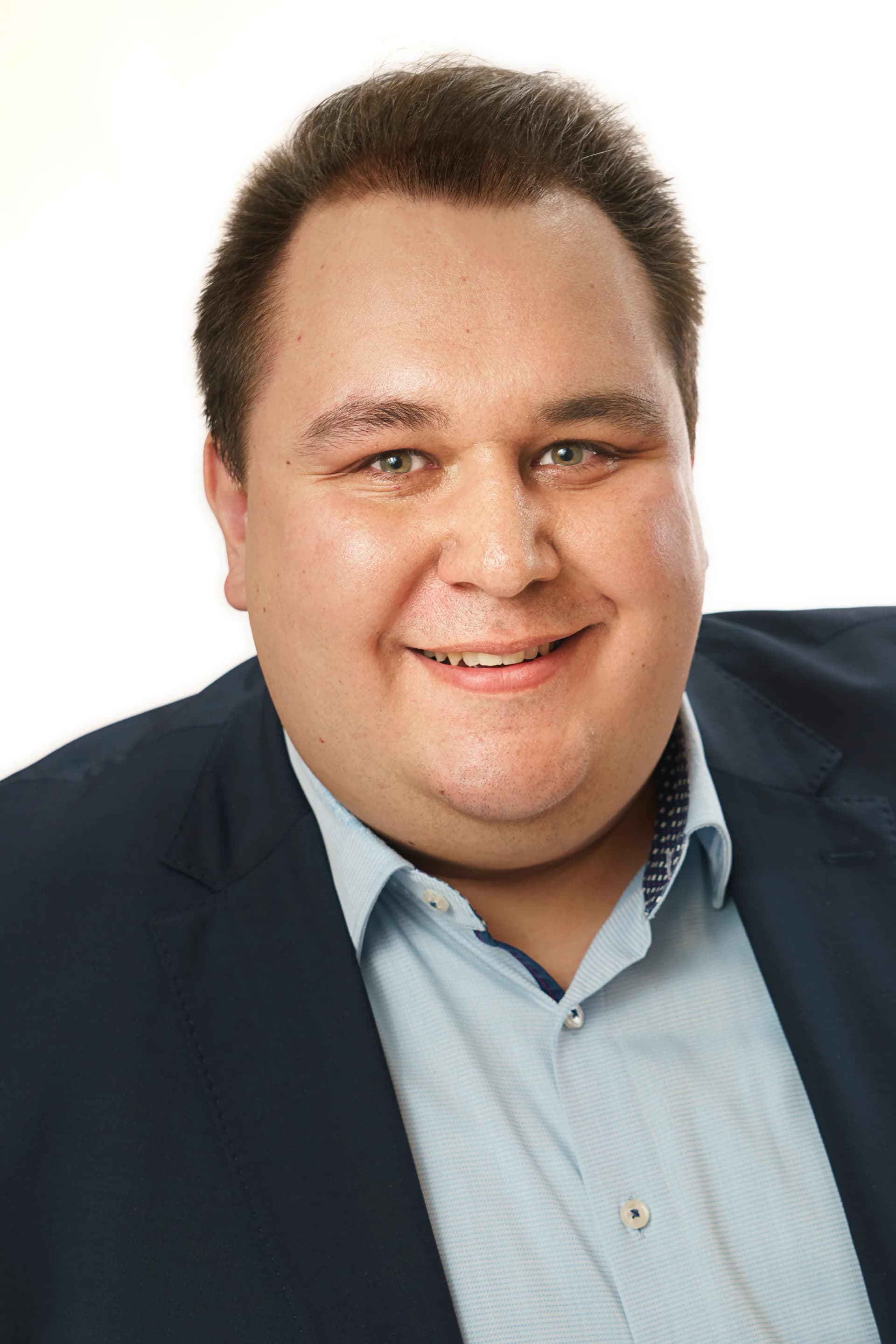 Porträt eines lächelnden Mannes mit kurzen braunen Haaren, dunklem Sakko und hellblauem Hemd vor weißem Hintergrund