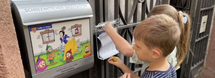 Kinder werfen einen Brief in den Schneewittchen-Briefkasten der Touristinfo Lohr a. Main ein.