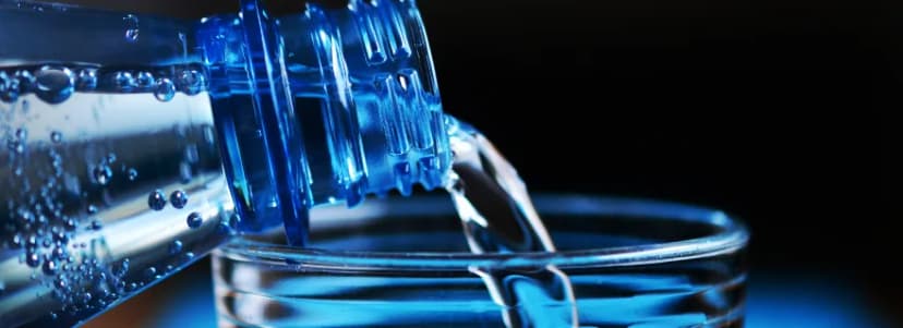 Wasser wird aus einer blauen Flasche in ein Glas gegossen.