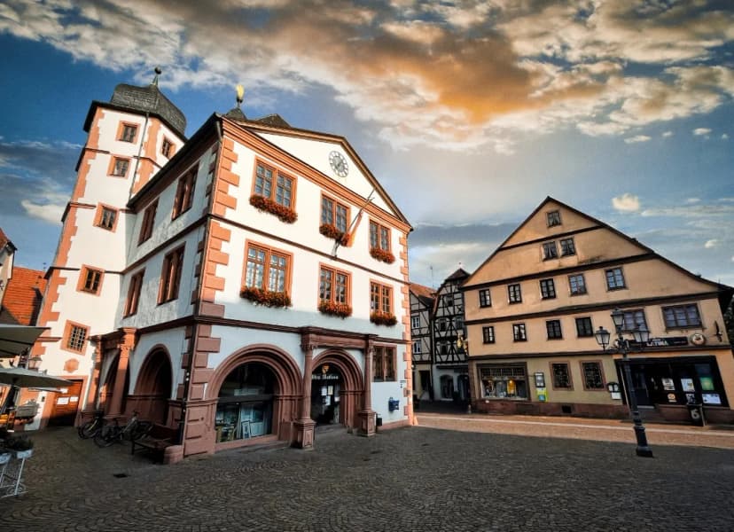 Altes Rathaus mit Turm und Blumenschmuck an den Fenstern am Marktplatz von Lohr am Main, im Hintergrund Fachwerkhäuser unter bewölktem Himmel