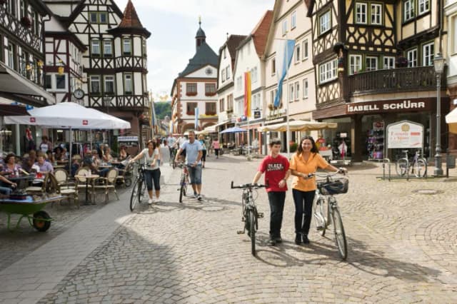 Fußgängerzone mit Fachwerkhäusern, Passanten mit Fahrrädern und Café-Tischen im Freien