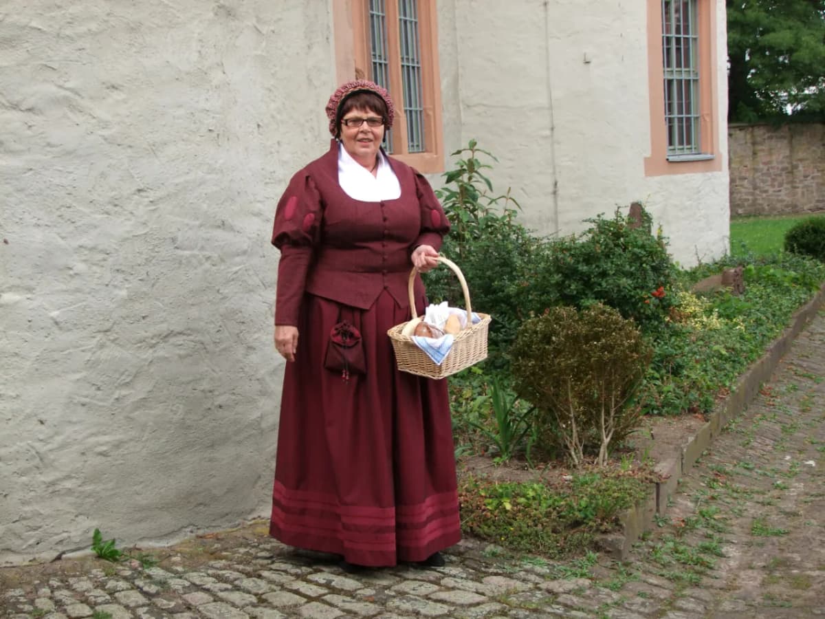 Eine Frau in einem historischen Bäckergewand mit Haube steht mit einem Korb mit Backwaren vor dem Schloss in Lohr am Main