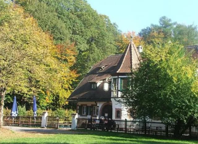 Gasthaus mit Turm und Fachwerk, umgeben von herbstlich gefärbten Bäumen, davor ein eingezäunter Biergarten