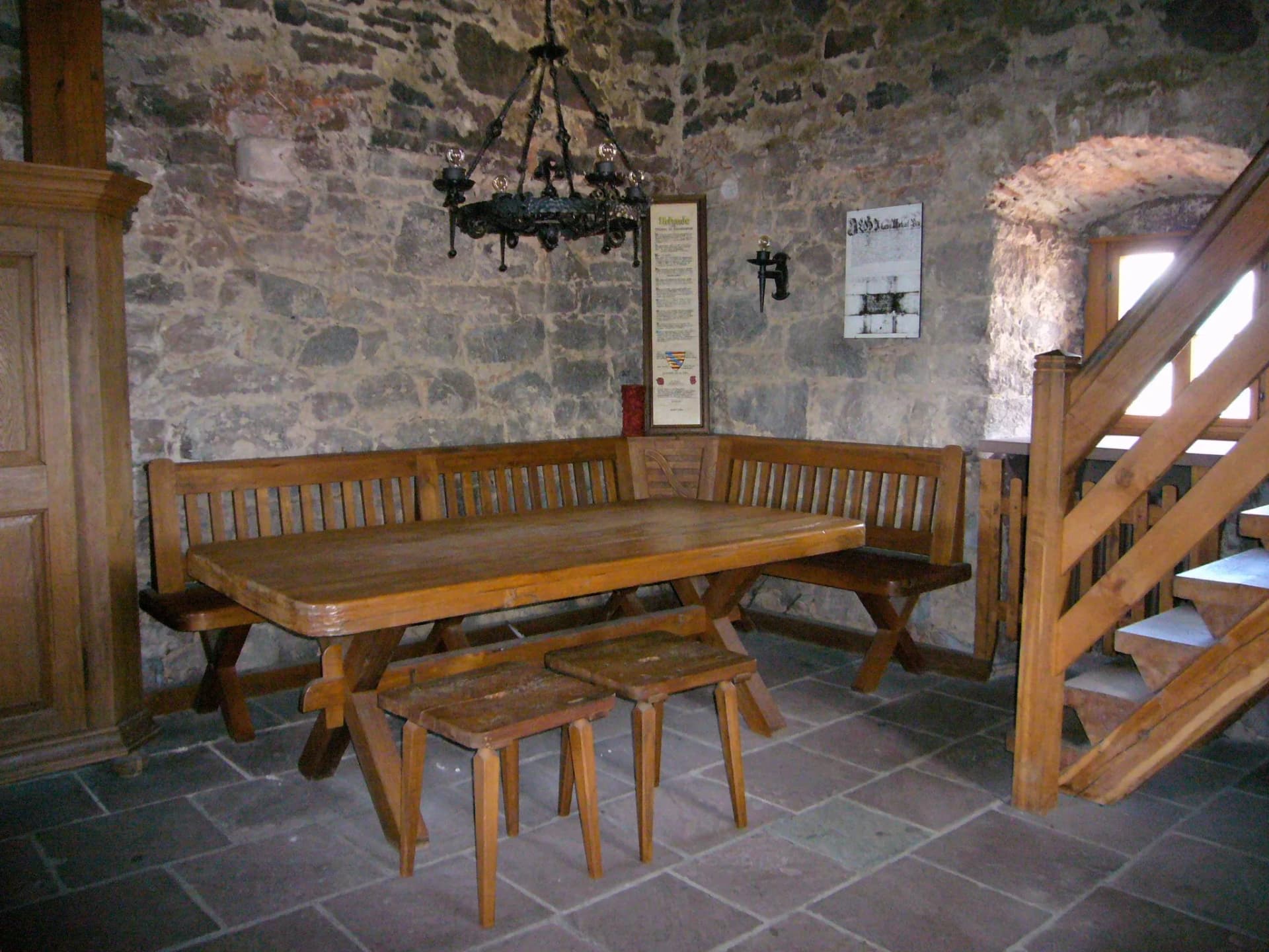 Rustikaler Raum mit Steinmauern, Eckbank und Holztisch, daneben eine Holztreppe