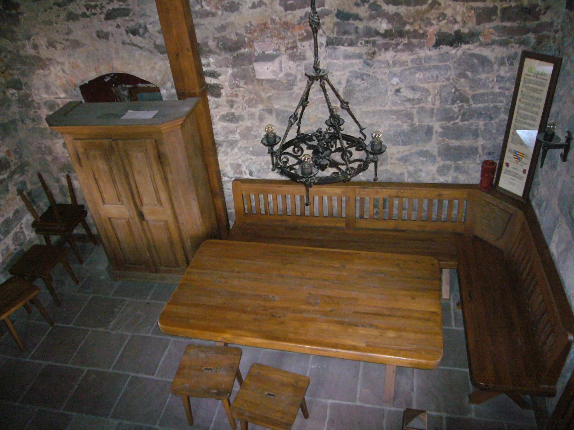 Historischer Raum mit Holztisch, Eckbank und schmiedeeisernem Kronleuchter vor Steinwand im Bayersturm.