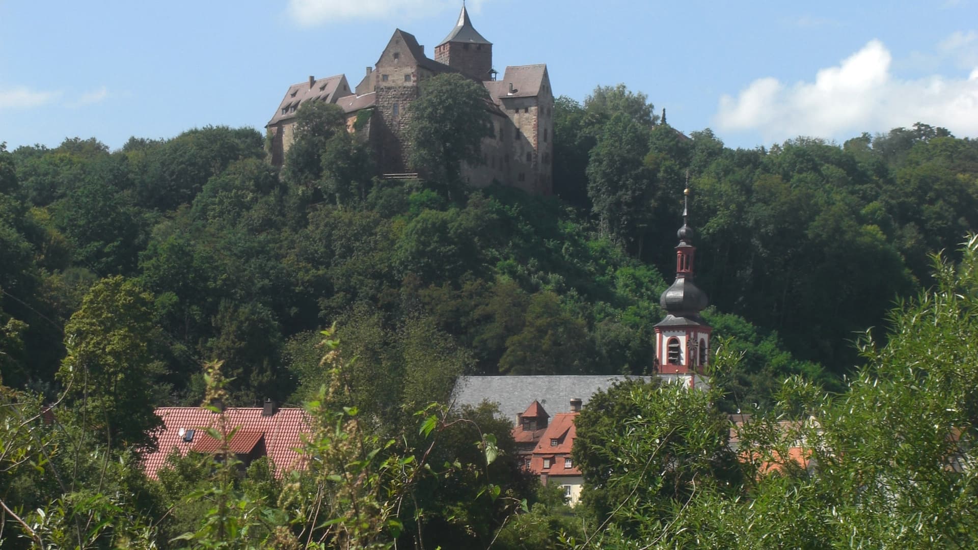 Blick auf die Burg Rothenfels in der kleinsten Stadt der Welt. Die Burg thront auf einer Anhöhe, im Vordergrund ist noch eine Kirche zu sehen.