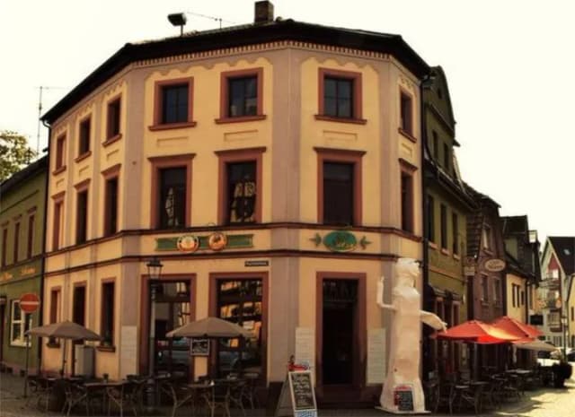 Eckhaus mit Café und Straßenterrasse, davor Sonnenschirme und eine weiße Statue