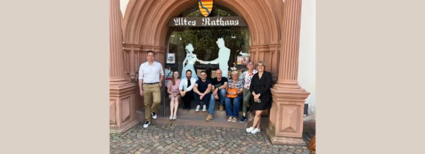 Gruppe von Personen sitzt und steht im Eingangsportal des Alten Rathauses vor einer gläsernen Tür mit Silhouettenmotiv.