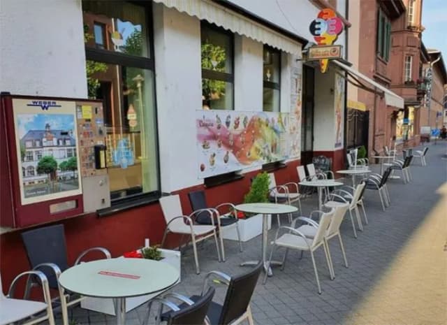 Eisdiele mit Sitzplätzen im Freien und Eiscreme-Werbeplakaten an der Hauswand