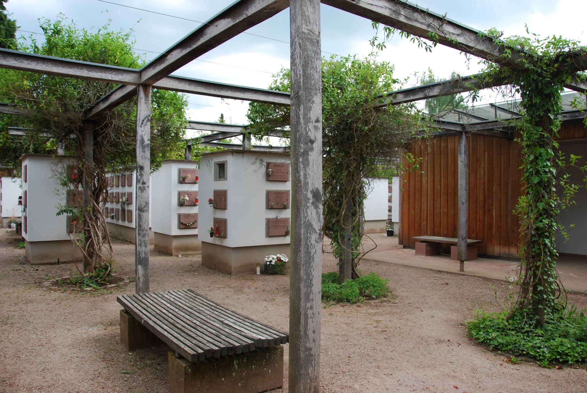 Urnenwand-Anlage mit begrünten Holzpergolen und Sitzbänken auf einem Friedhof