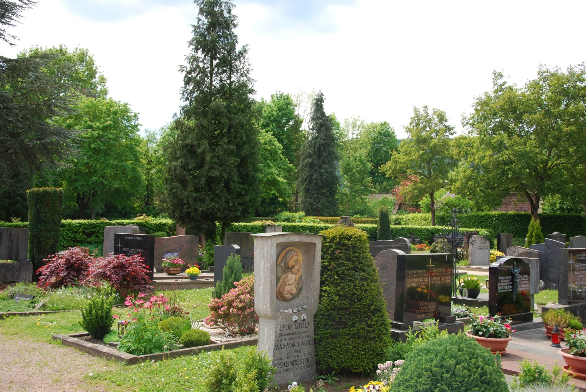 Friedhof mit Grabsteinen, Blumenschmuck, Hecken und Bäumen