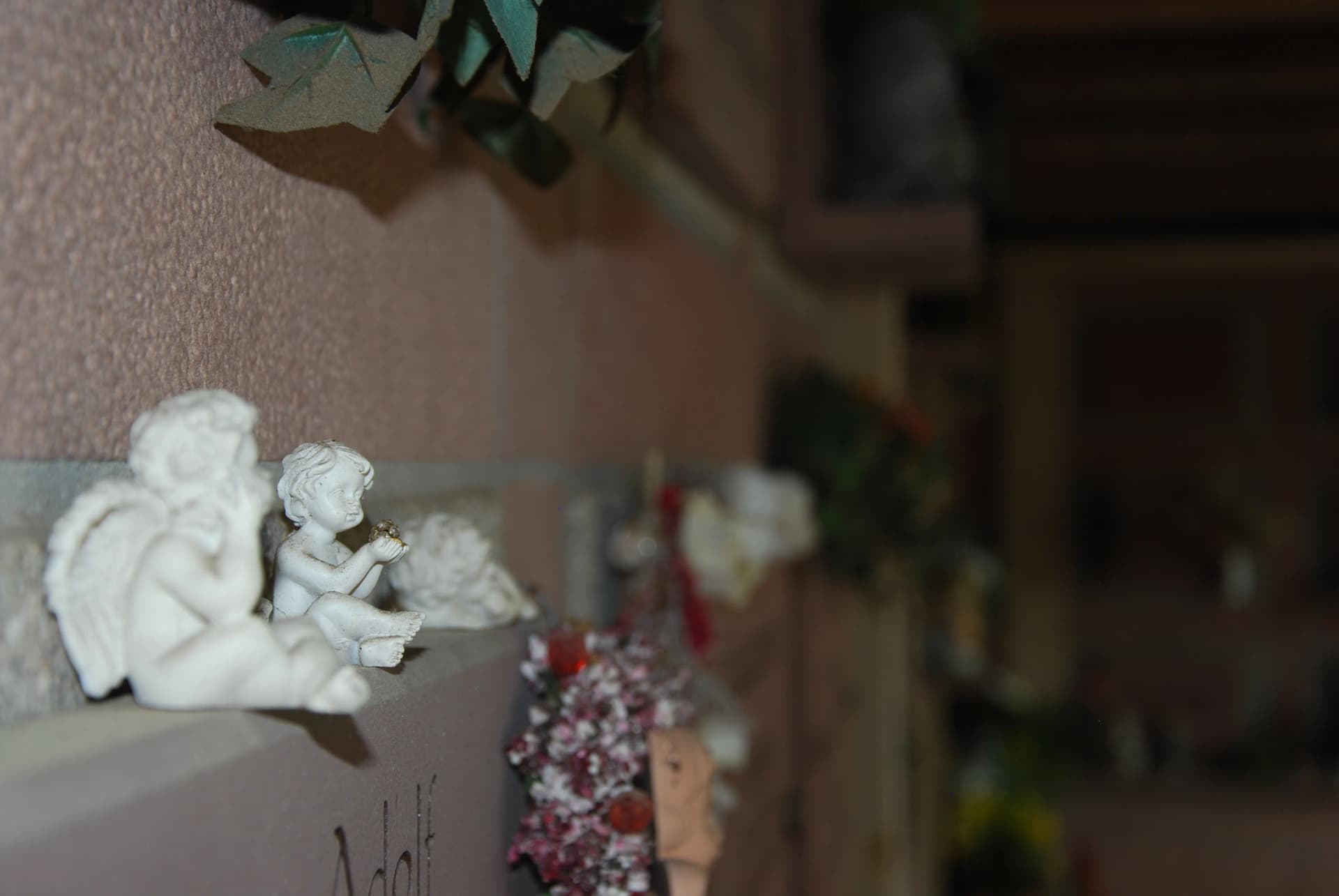 Kleine Engelsfiguren aus Stein auf einem Grabstein, umgeben von Blumenschmuck und Efeu
