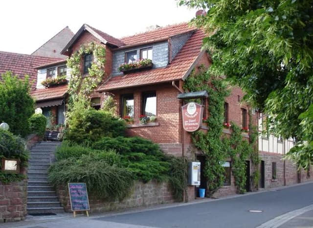 Backsteinhaus mit Efeu und Blumenkästen, Gasthaus Dorfbrunnen mit Schild und Kreidetafel an der Straße