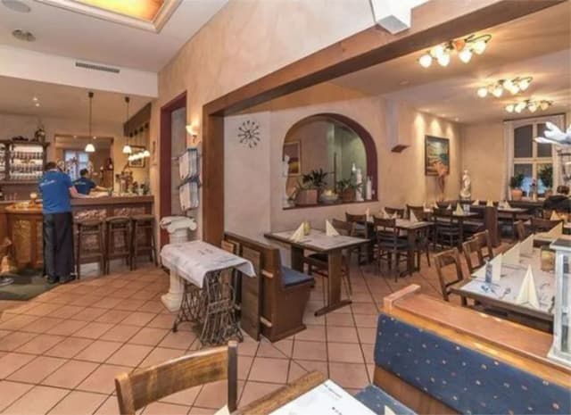 Innenraum eines Restaurants mit gedeckten Tischen, Holzstühlen und Theke im Hintergrund
