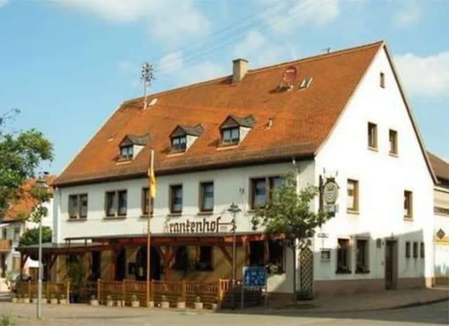Gasthaus Frankenhof mit weißer Fassade, rotem Ziegeldach und Gaststättenterrasse im Erdgeschoss