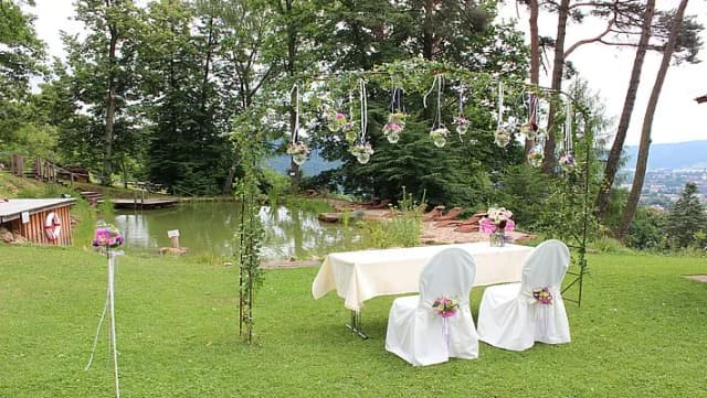 Festlich dekorierter Platz im Garten mit Tisch, weißen Stuhlhussen und Blumenschmuck neben einem Teich