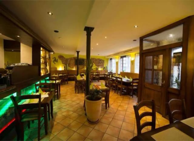 Innenraum eines Restaurants mit gedeckten Holztischen, Theke und Fliesenboden