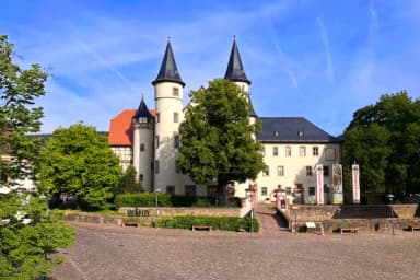 Schloss mit zwei Türmen und Fachwerkgiebel, davor ein gepflasterter Platz mit Bäumen