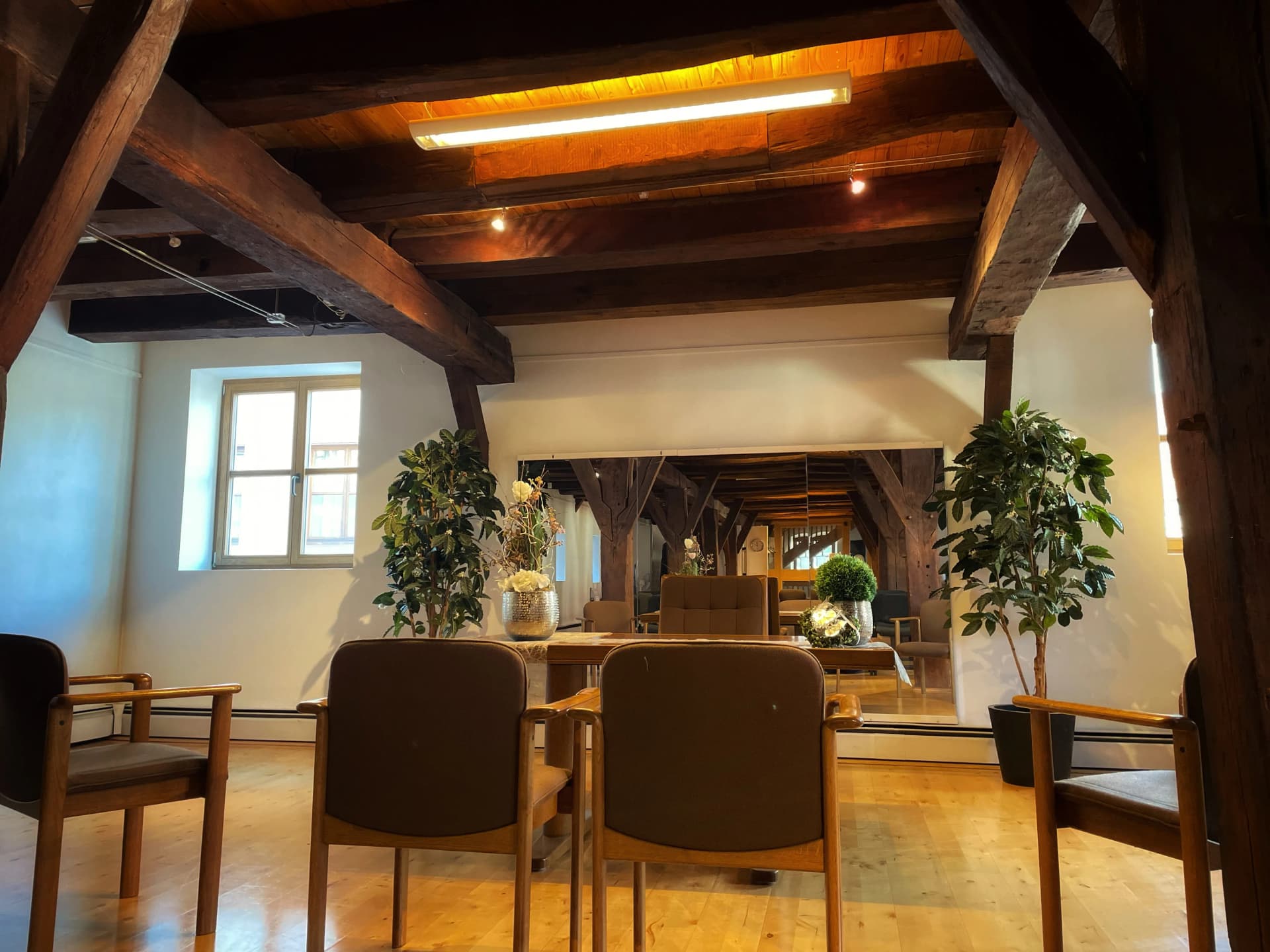 Dachgeschossraum mit freiliegenden Holzbalken, Sitzgruppe aus Stühlen und Tisch sowie Grünpflanzen in der Kellereischeune